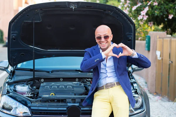 Uomo che mostra il gesto della mano del cuore in piedi vicino alla sua auto con cappuccio aperto — Foto Stock