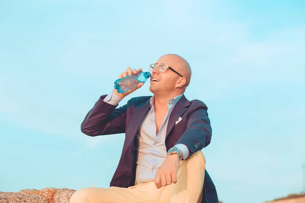 Uomo in occhiali che beve un'acqua fuori seduto su rocce all'aperto — Foto Stock