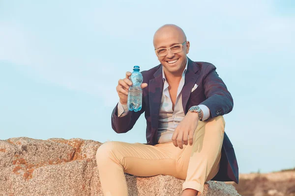 Uomo dandovi acqua in bottiglia fuori isolato seduto su rocce — Foto Stock