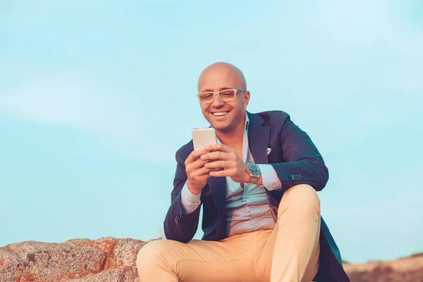 Hombre mirando el teléfono móvil sentado en las rocas al aire libre — Foto de Stock