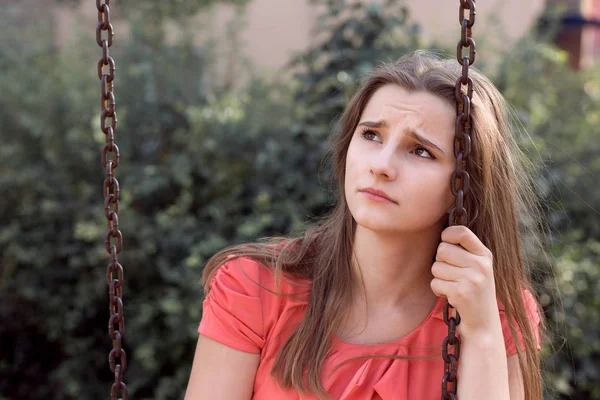 Triste menina adolescente infeliz com longo cabelo morena sentado em um balanço, infelizmente, olhando para cima — Fotografia de Stock
