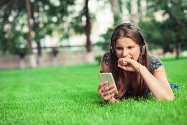 Genç kadın bir korku hayal kırıklığı içinde dışında telefon ekranýnda kopya alanı yeşil çim zemin üzerine uzanarak park bakarak yumruk ısır. Çok kültürlü modeli karışık yarış Asyalı Rus genç kız