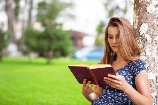 若い魅力的な女性の背景に緑の芝生ツリーのキャンパスに座りながら本を読んで勉強します 多文化共生 混合レース アジアのロシアの女の子 水平方向ショット 人と文学の概念 ストックフォト