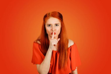 Sessiz jest. Kırmızı arka planda izole edilmiş dudaklara parmağını koyan genç bir kadının yakın çekimi.