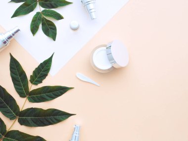 Doğal kozmetik konsepti. Taze yeşil yapraklar, yüz, göz kremi, duş jeli, sıvı sabun, bej rengi çıplak ten arka planında izole edilmiş beyaz kağıt üzerindeki spa taşları. Düz konum, üst görünüm kopyalama alanı. 