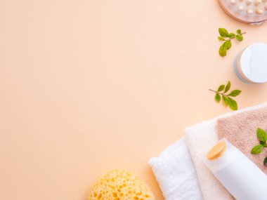 Doğal kozmetik konsepti. Taze yeşil fesleğen yaprakları, vücut jeli, şampuan, masaj aleti, fırçalama eldiveni ve havlular pastel bej rengi çıplak ten arka planda izole edilmiş. Düz konum, üst görünüm, kopyalama alanı