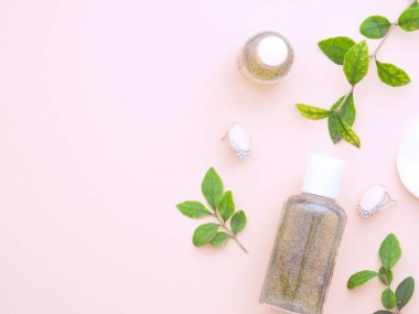 Taze yeşil yapraklar, doğal kozmetik ürünler, vücut jeli ya da sıvı el yapımı sabun, küpeler ve pastel pembe arka planda izole edilmiş pamuk pedi. Minimalist tasarım. Düz konum, üst görünüm, kopyalama alanı