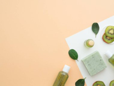 Doğal kozmetik konsepti. Taze yeşil yapraklar kivi dilimleri, vücut jeli sıvı el yapımı sabun beyaz kağıt üzerinde meyvemsi aromalı çıplak ten rengi bej arka plan. Düz görünüm kopyalama alanı