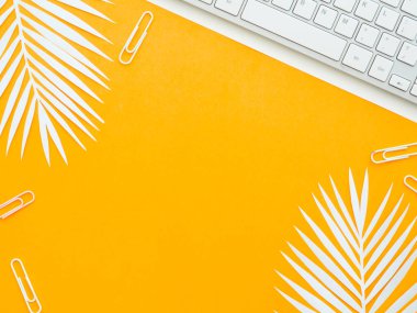 Üzerinde beyaz eğrelti otu yaprakları olan sarı turuncu iş yerinde izole edilmiş beyaz kağıt üzerinde bir klavye. Yaratıcı çalışma alanı.