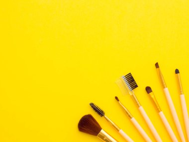 Makyaj fırçaları sarı arka planda izole edilmiş bir köşede kopyalanmış araçlar. Yatay görüntü, düz konum, yukarıdan üst görünüm