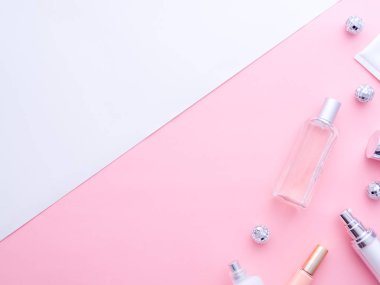 Kadın moda güzellik blogcusu çalışma alanı. Makyaj malzemeleri, kozmetik, parfüm, krem şişeleri, yarı pembe yarı beyaz fotokopi arka planında izole edilmiş Noel topları. Üst görünüm