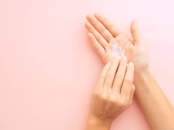 Woman hands applying cream isolated on pastel pink background with copysace. Horizontal image, flat lay, top view from above