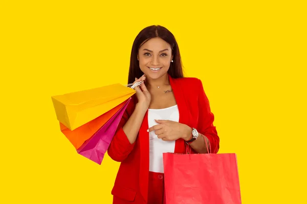 Beautiful woman with shopping bags looking at you camera smiling. Mixed race model isolated on yellow background with copy space. Horizontal image. Natural, no makeup.