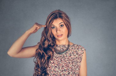 Sinirli genç bir kadının yakın plan portresi. Parmağıyla tapınağa doğru hareket ediyor. Deli misin diye soruyor. Arka planda gri bir duvar var. Negatif duygular yüz ifadesi vücut dilini hissetmek