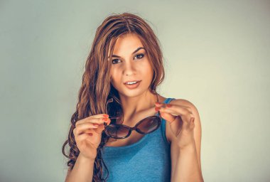 Yakın plan portresi. Genç, güzel, gülümseyen bir kız. Güneş gözlüğü takıyor ve yeşil arka plan mavi gömleğine bakıyor. Olumlu duygu yüz ifadesi vücut dili