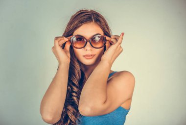 Yakın plan portre portresi açık yeşil arka plan duvarında izole edilmiş güneş gözlüklerine dokunan seksi, mutlu genç bir kadın. Pozitif insan duyguları ifade ile yüzleşir. Hayatı algılama güzellik kavramını hissetmek.