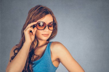 Yakın plan portre, kendine güvenen, başarılı, güzel, çekici genç kadın, moda kızı, güneş gözlüğü takan bir kız, izole edilmiş gri arka plan duvarı. Pozitif insani duygu, yüz ifadesi