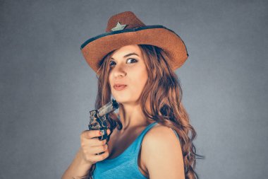 Kovboy şapkalı kadın çifte namlulu silahla kameraya nişan alırken şaşırdı. Gri arka planda izole edilmiş karışık ırk modeli ve kopyalama alanı. Yatay resim.