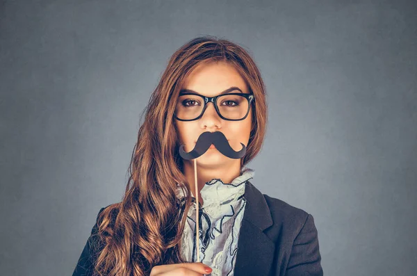 Ciddi bir erkeği taklit eden güzel, güzel, genç bir kadının portresini yakından çek. Gri arka planda sahte bıyıklı çekici bir kız. Olumlu insan duyguları, yüz ifadeleri