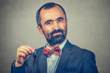 Ciddi sakallı bir adamın portresi, kırmızı papyonlu zarif bir ceket giyiyor ve arka planda gri bir duvar var. İnsan yüzü ifadesi