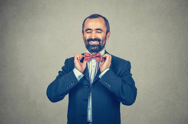 Homem feliz, barbudo com terno escuro, camisa azul, ajustando o arco borboleta vermelho, gravata. Sorrindo, gerente elegante. Emoção humana positiva. Um acessório. Fundo de parede cinza . — Fotografia de Stock