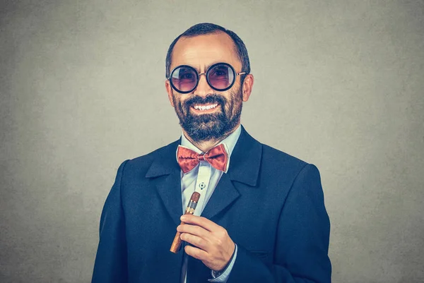 Sorrindo, confiante, homem barbudo usar óculos de sol redondos, manter o charuto cubano. Retrato de elegante, cara engraçado olhando para você câmera. Oftalmologia. Roupas modernas, terno escuro, camisa, arco vermelho, gravata. Emoção . — Fotografia de Stock