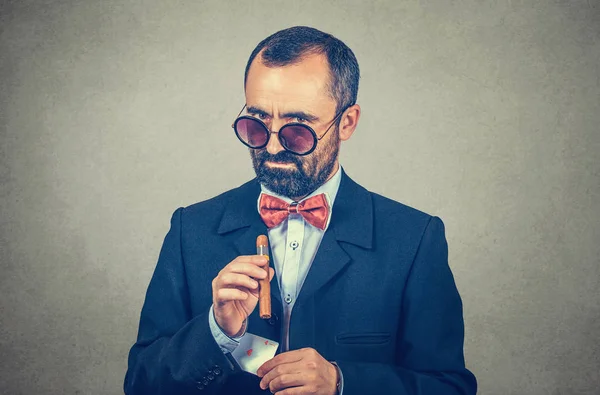 Hombre mirando por encima de las gafas de sol con un cigarro sacando un as de su slleve — Foto de Stock