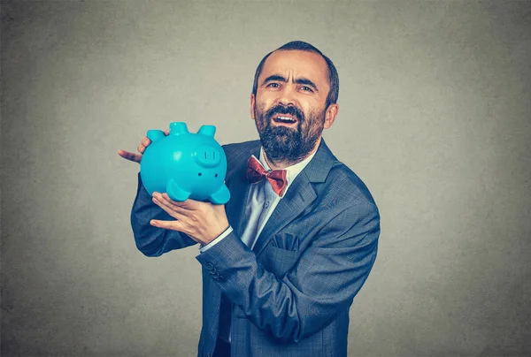 Erwachsener, enttäuschter bärtiger Mann im eleganten Anzug mit roter Fliege und umgestürztem Sparschwein, das seine Leere zeigt, isoliert auf dem grauen Wandhintergrund. — Stockbild Enttäuschter Mann mit umgekipptem Sparschwein, das seine Leere zeigt — Stockfoto
