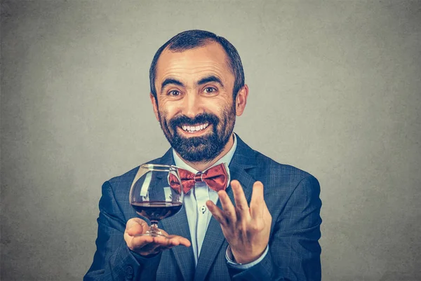 Улыбающийся взрослый бородатый мужчина в элегантной куртке с красной бабочкой и бокалом вина, подсчитывающий на пальцах количество выпитого и смотрящий в камеру, изолированный серый фон. Позитивное человеческое выражение . — стоковое фото