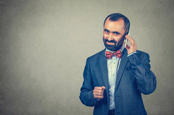 Homem adulto sorridente beared vestindo terno elegante e camisa com gravata borboleta vermelha, falando no telefone celular isolado no fundo da parede cinza. Expressão humana positiva, linguagem corporal — Fotografia de Stock