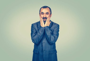 Mutlu yetişkin yakışıklı adam şaşırmış görünüyor. İnanmayan eller yanakta açık ağız gözler, izole edilmiş açık yeşil duvar arka planı. Olumlu insani duygular, yüz ifadeleri, duygular,