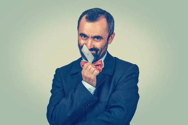 Bearded businessman scratch, touch his nose with ace card ��� liar, thump concept. Human face expressions. Isolated man looking sly to you camera. Gray wall background. — ストック写真