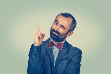 Mature businessman winking pointing up looking at camera cheerful. Mixed race bearded model isolated on green yellow studio background with copy space. Horizontal image.
