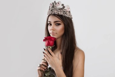 Beautiful like a flower. Woman holding a red rose looking at you the camera isolated white background. Brunette dark hair and skin trendy makeup shiny lips eye shadow in combination set burgundy nails