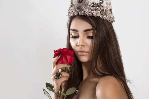 Dark beauty with flower. Mysterious queen crowned woman eyes closed holding a red rose in her hand on white gray background. valentine shiny lips burgundy nails beautiful luxury makeup and manicure — ストック写真