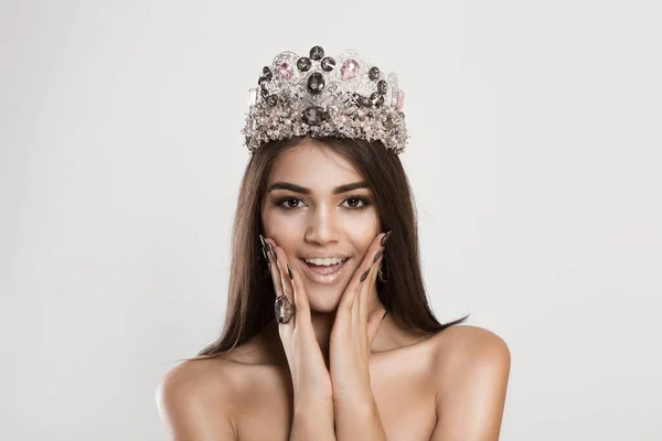 Wow. Close up portrait happy dark beauty queen young indian woman with crown beautiful girl looking excited holding her mouth opened hands on cheeks on white gray wall. Shocked surprised stunned
