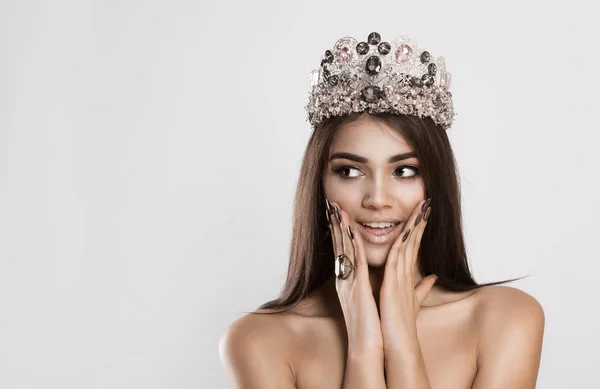 Ena! Uma rainha da beleza feliz e surpresa coroado modelo de moda mulher olha para suas mãos direitas em seu rosto bochechas contra um fundo cinza branco — Fotografia de Stock