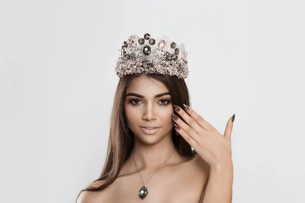 Beautiful & happy. Beauty crowned queen girl woman actress miss bride to be hand near face smiling showing manicure looking at camera white wall. Full makeup diamond silver black pink crystals crown