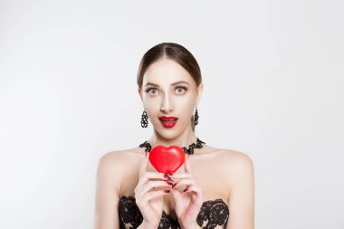 The girl showing the affection, holds the heart in her hands, the expression of the girl is a little surprise, amazing isolated white background. Red heart box, lips and black dress earrings chokers