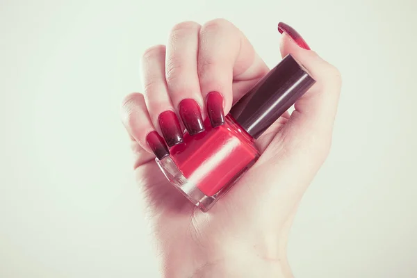 Mujer sosteniendo botella de esmalte de uñas. Manicura artística. Gradiente de estilo moderno rojo negro esmalte de uñas. Elegante estilete colorido Clavos aislado fondo blanco. Hermosa mano femenina con manicura de belleza — Foto de Stock