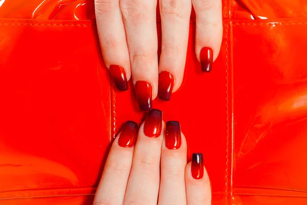 Nail Polish. Art Manicure. Modern style red black gradient Nail Polish. Stylish Colorful trendy Nails beauty hands isolated red bag as a background — Stock Photo, Image