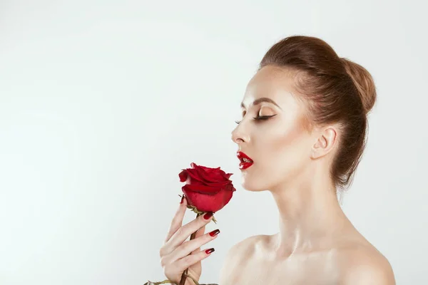 Hermosa como una rosa. Niña sosteniendo rosa flor en perfil vista lateral aislado gris claro fondo blanco. Belleza Modelo Mujer Rostro ojos cerrados con labios rojos y uñas. Piel perfecta. Maquillaje profesional — Foto de Stock