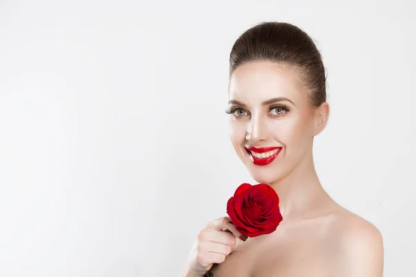 Bella come un fiore.. Donna felice in possesso di una rosa rossa, sorridente guardandoti la fotocamera isolato sfondo bianco. Bruna, capelli scuri, ciglia finte trucco naturale rosso nero gradiente labbra unghie — Foto Stock