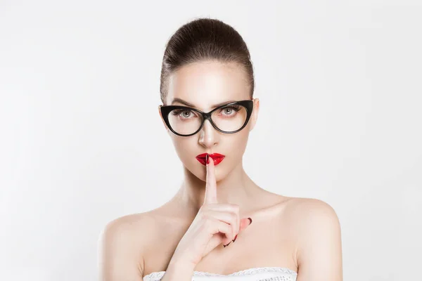 Mujer enojada hermosa con las cejas de las gafas levantadas pidiendo silencio o secreto dedo en los labios silencio gesto de la mano aislado pared de fondo blanco. Shhh quietud es signo secreto símbolo Expresión de la cara — Foto de Stock