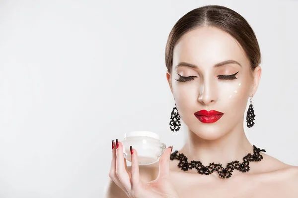 Drops of cream on face. Beautiful model showing applying cosmetic cream treatment on her face on white grey. Closeup portrait of woman with nourishing hydrating cream and bottle in hand eyes closed — Stockfoto