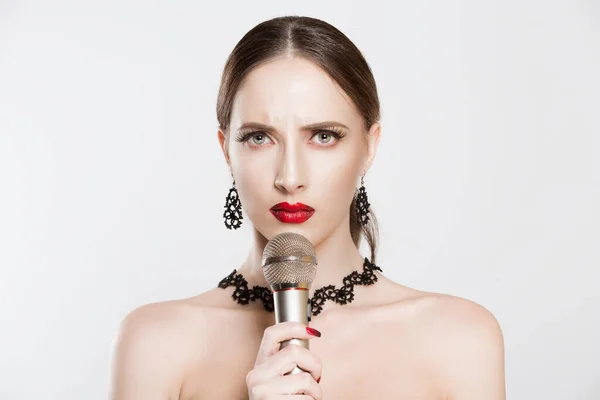 Girl, Miss actress angry talk at mic against racism and war. Young attractive unhappy worried woman thinking about song with microphone in hand, beautiful makeup against white background.