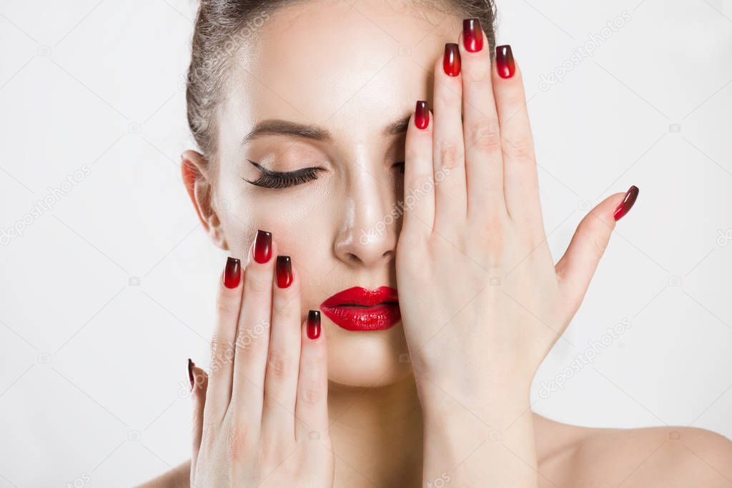 Red and black gradient nails and lips combination set. Beautiful young woman covering her eye with her hand, nude makeup false eyelashes, nails done, red lipstick