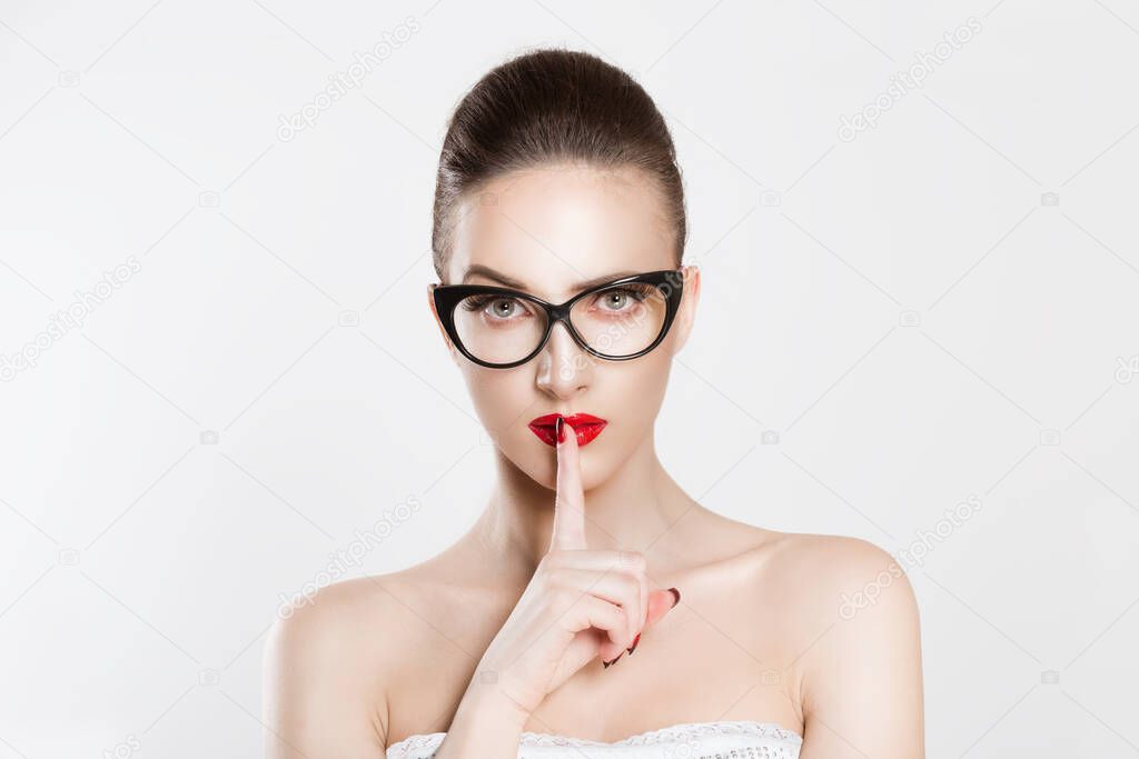 Beautiful angry Woman with eyeglasses eyebrows raised asking for silence or secrecy finger on lips hush hand gesture isolated white background wall.  Shhh quiet it's secret sign symbol Face expression