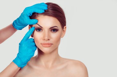 Upper eyelid blepharoplasty. Beautiful middle age woman getting ready for eyelid lift plastic surgery doctor hands in blue gloves point fingers to her eye on white. Beauty, people and health concept clipart