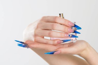 Tırnak cilası. Sanat manikürü. Modern tarz mavi oje. Güzel eller parfüm şişesini tutuyor. Renkli stil stiletto Çiviler izole edilmiş beyaz arkaplan